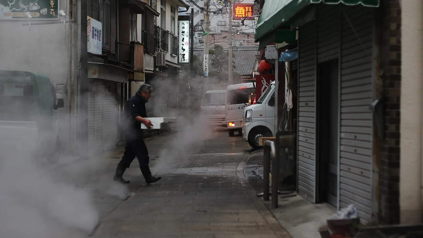 Beppu's cityscape under drifting columns of hot spring steam, hills rising behind the bay