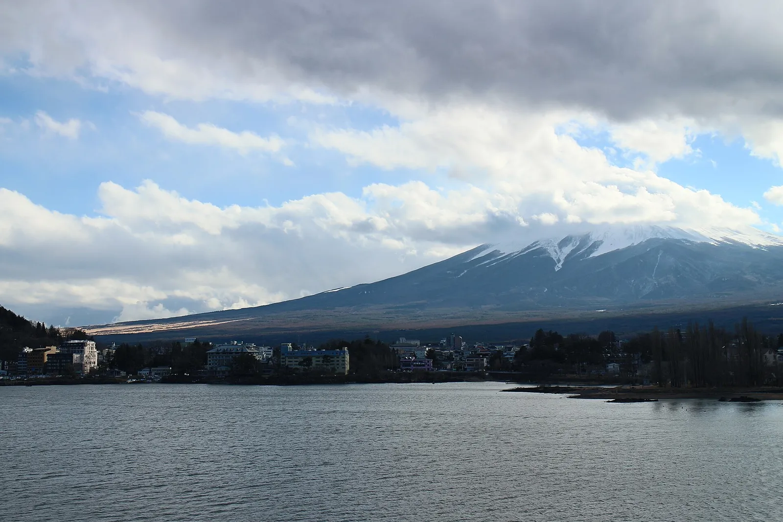 Mount Fuji rising behind a lake town, seen from a shinkansen-window vantage point on a clear day