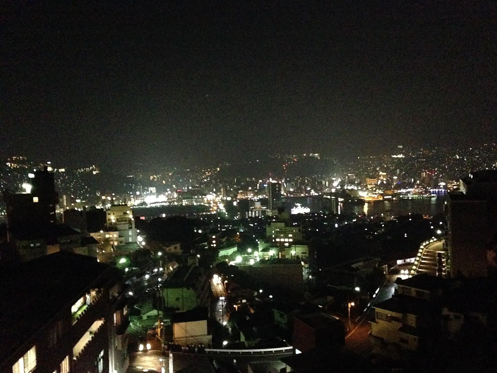 Nagasaki harbor seen from the water at dusk, hillsides rising around the port