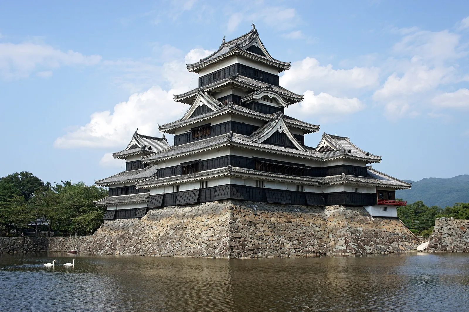 The black five-story keep of Matsumoto Castle rising above its stone moat under a clear sky